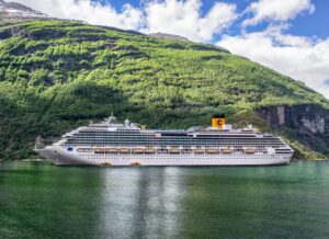 Costa Favolosa Cruise Ship in Scenic Norwegian Fjord Large white cruise ship “Costa Favolosa” sailing through a calm green fjord surrounded by steep forested mountains under a partly cloudy sky.